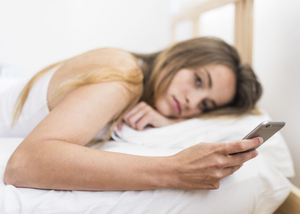 Mujer buscando en internet tratamiento de ansiedad y depresión tumbada en la cama. 
